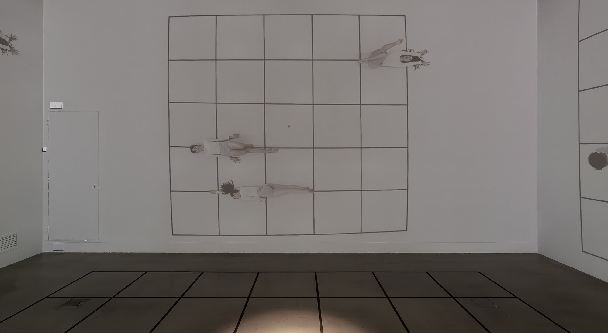 Dancers lying across a projected grid as though on a floor turned upright