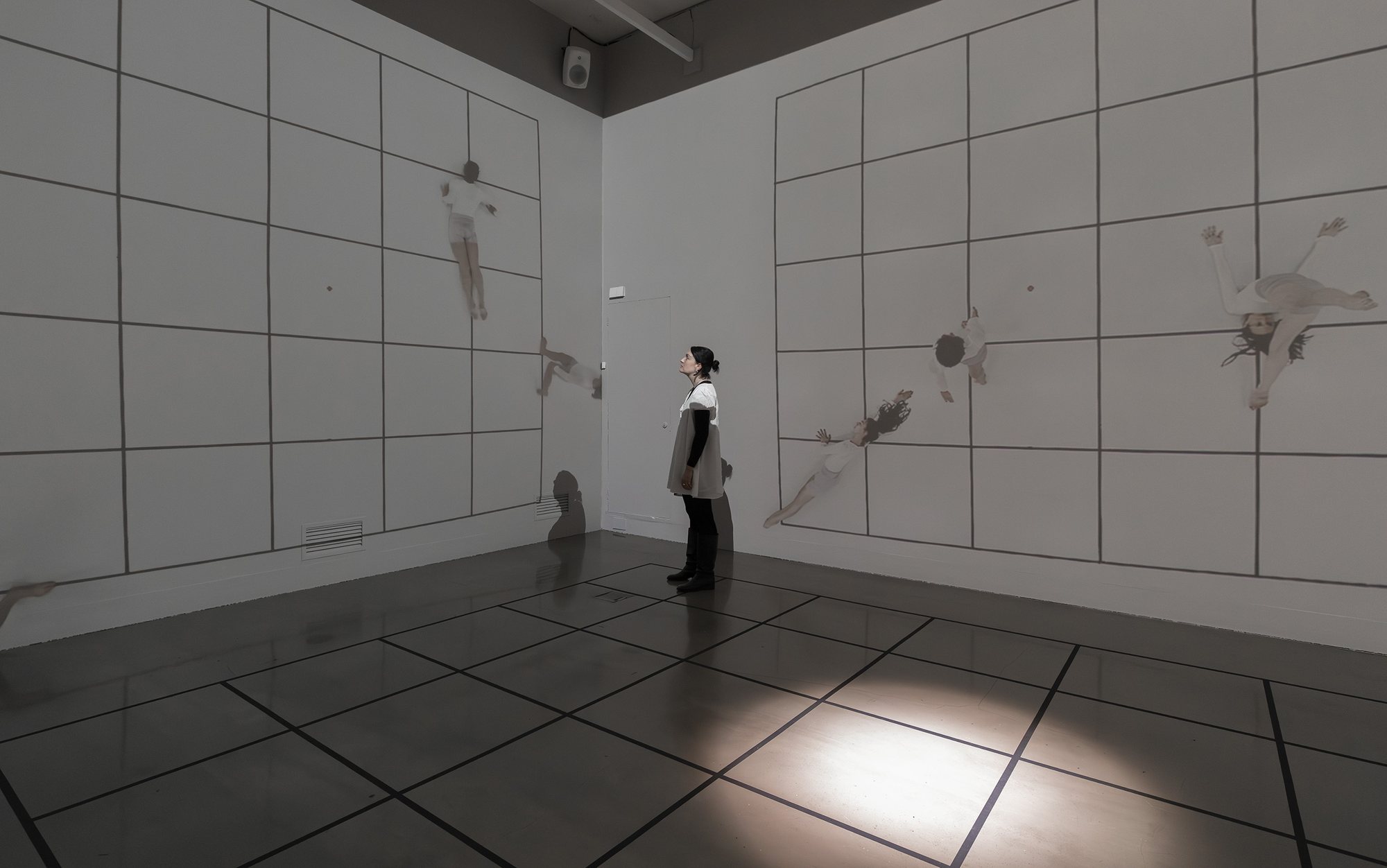 A visitor stands between two walls of projected dancers seen from above on a drawn grid
