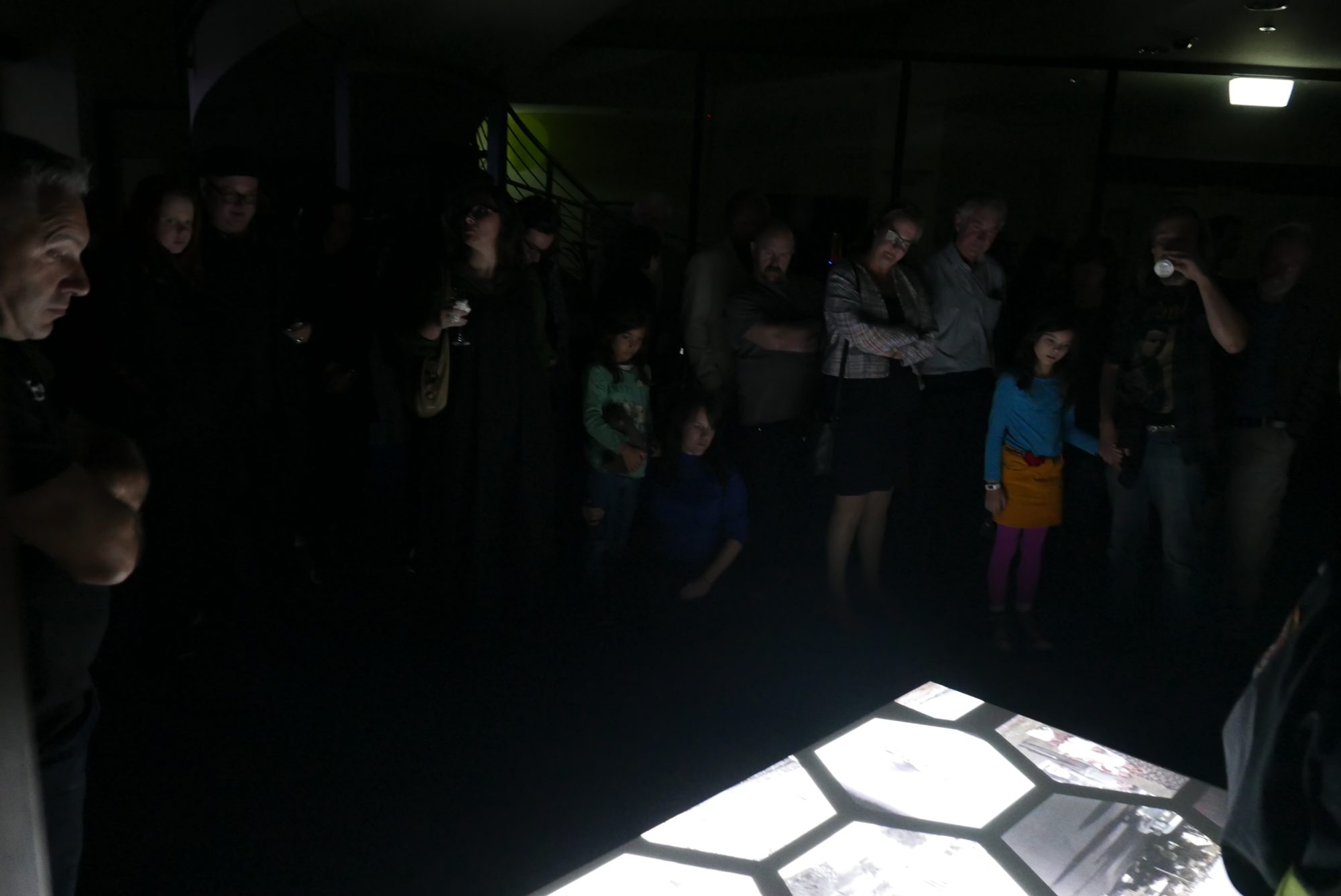 Visitors in the dark round the projected honeycomb of videos