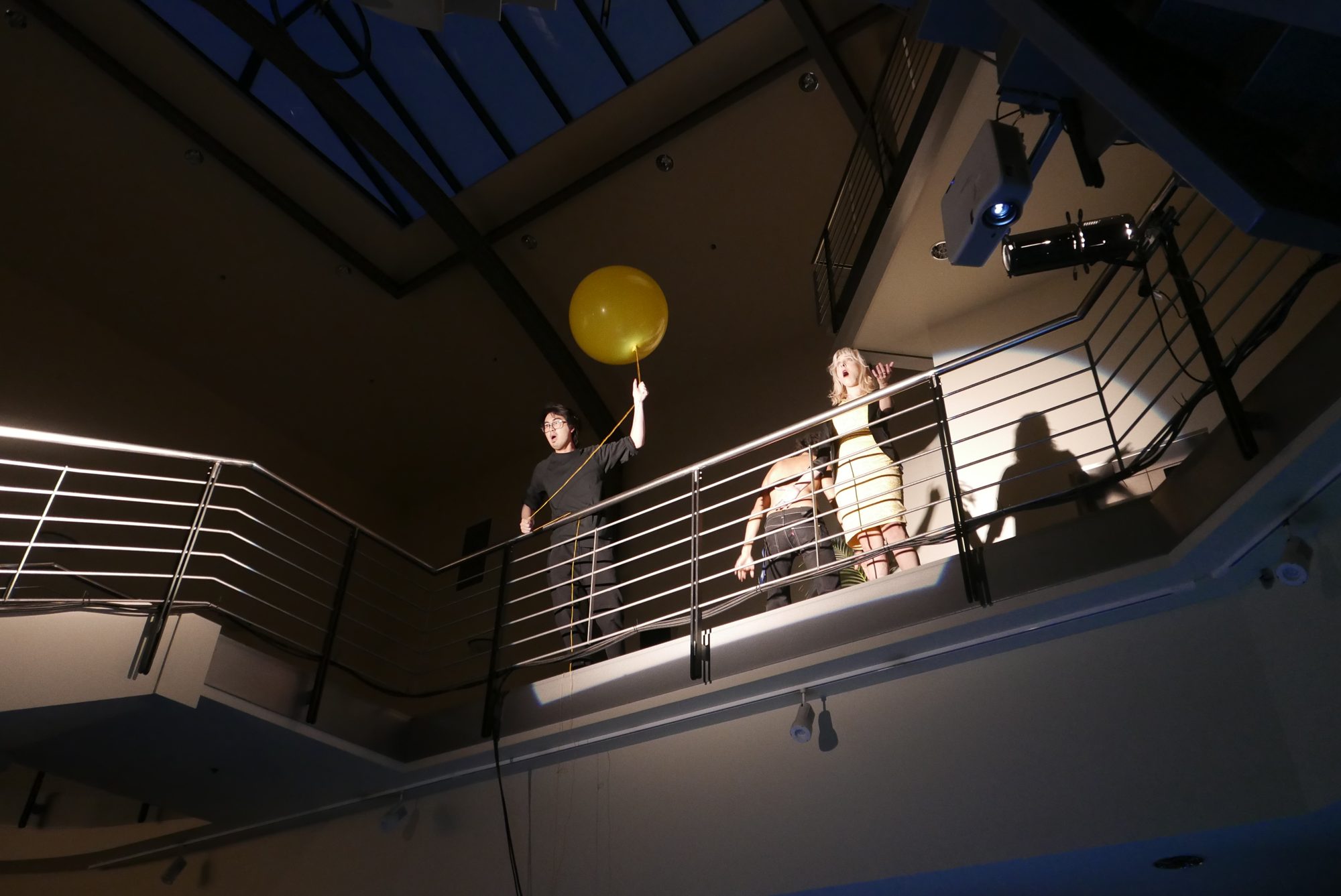 A performer holds a yellow balloon on the upper landing of the atrium