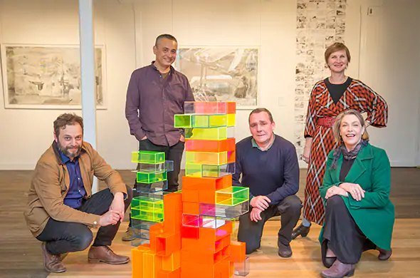 Five researchers with a stacked sculpture of coloured acrylic blocks in the Iconic Industry exhibition